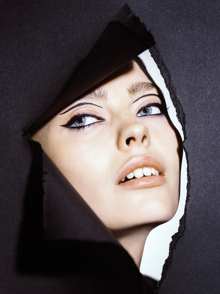 Model schaut durch schwarze Papierwand mit geometrischem Eyeliner