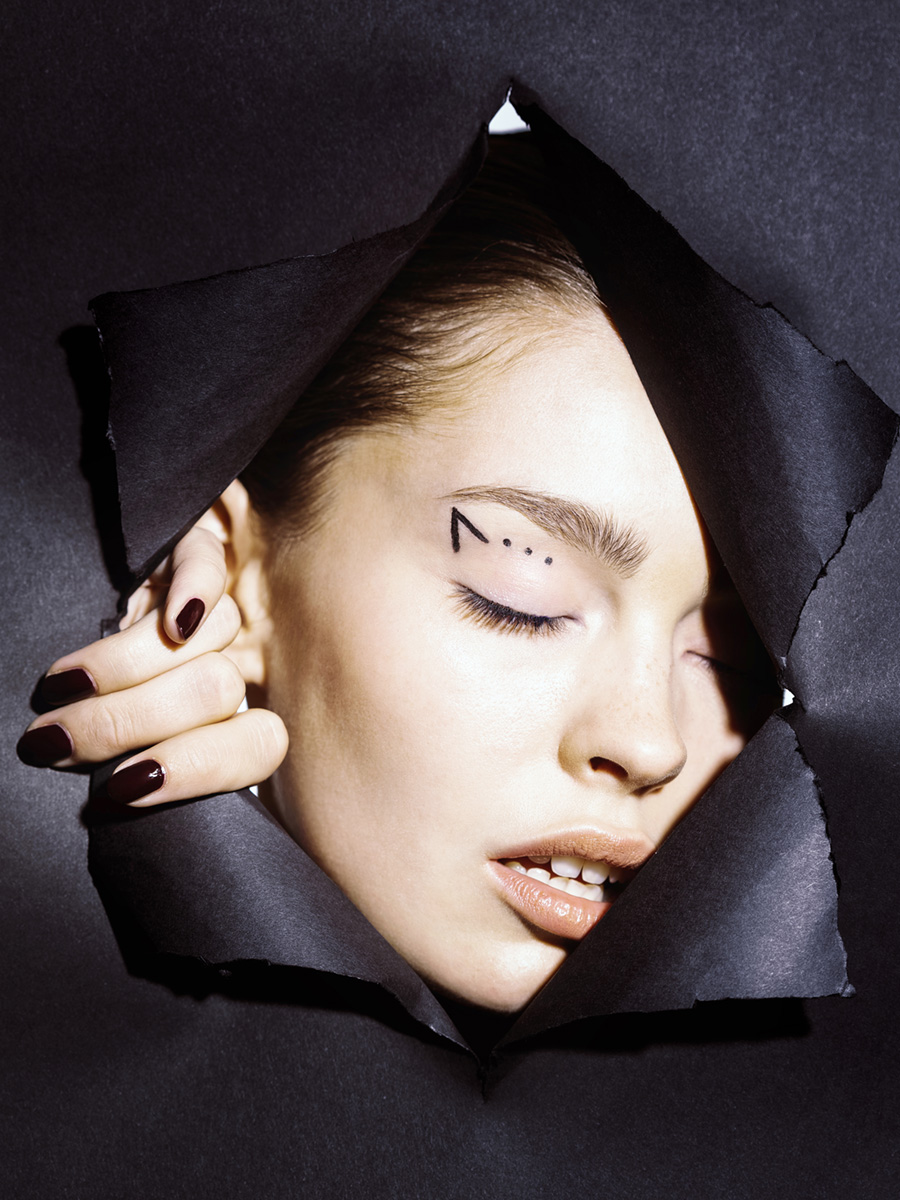 Model schaut durch schwarze Papierwand mit geometrisch geschminkten Augen
